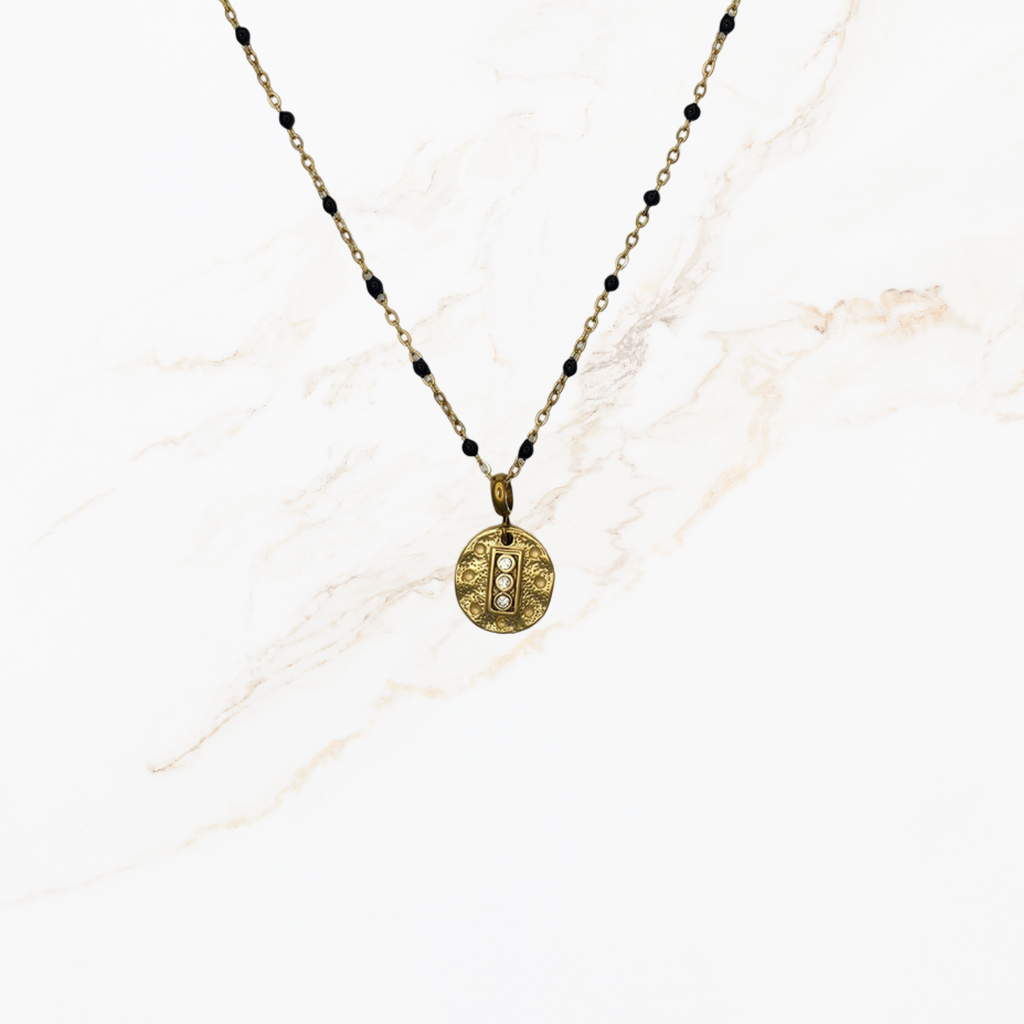 Goudkleurige ketting met kleine zwarte kraaltjes voor het samenstellen van een ketting met bedels op lichte marmer achtergrond.