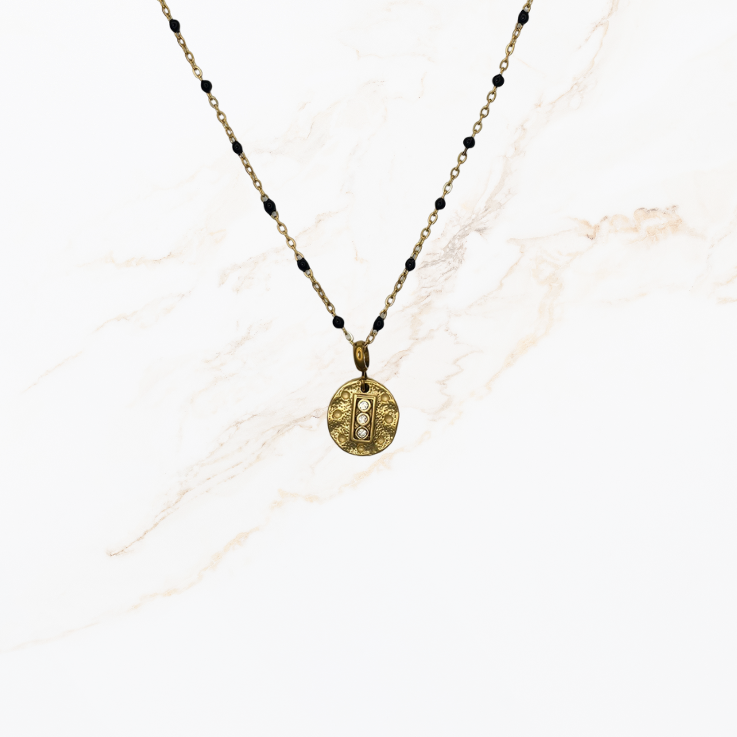 Goudkleurige ketting met kleine zwarte kraaltjes voor het samenstellen van een ketting met bedels op lichte marmer achtergrond.