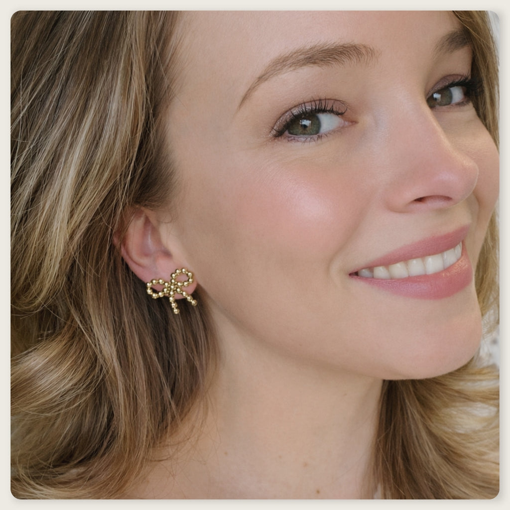 Seyso goudkleurige statement oorbellen in strikvorm met ronde bolletjes op lichte marmerlook achtergrond