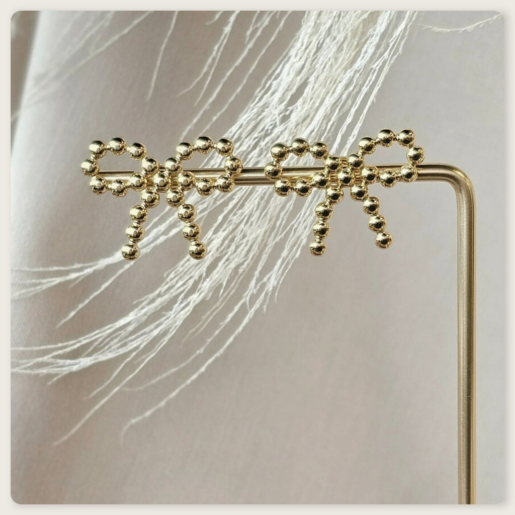 Seyso goudkleurige statement oorbellen in strikvorm met ronde bolletjes op lichte marmerlook achtergrond