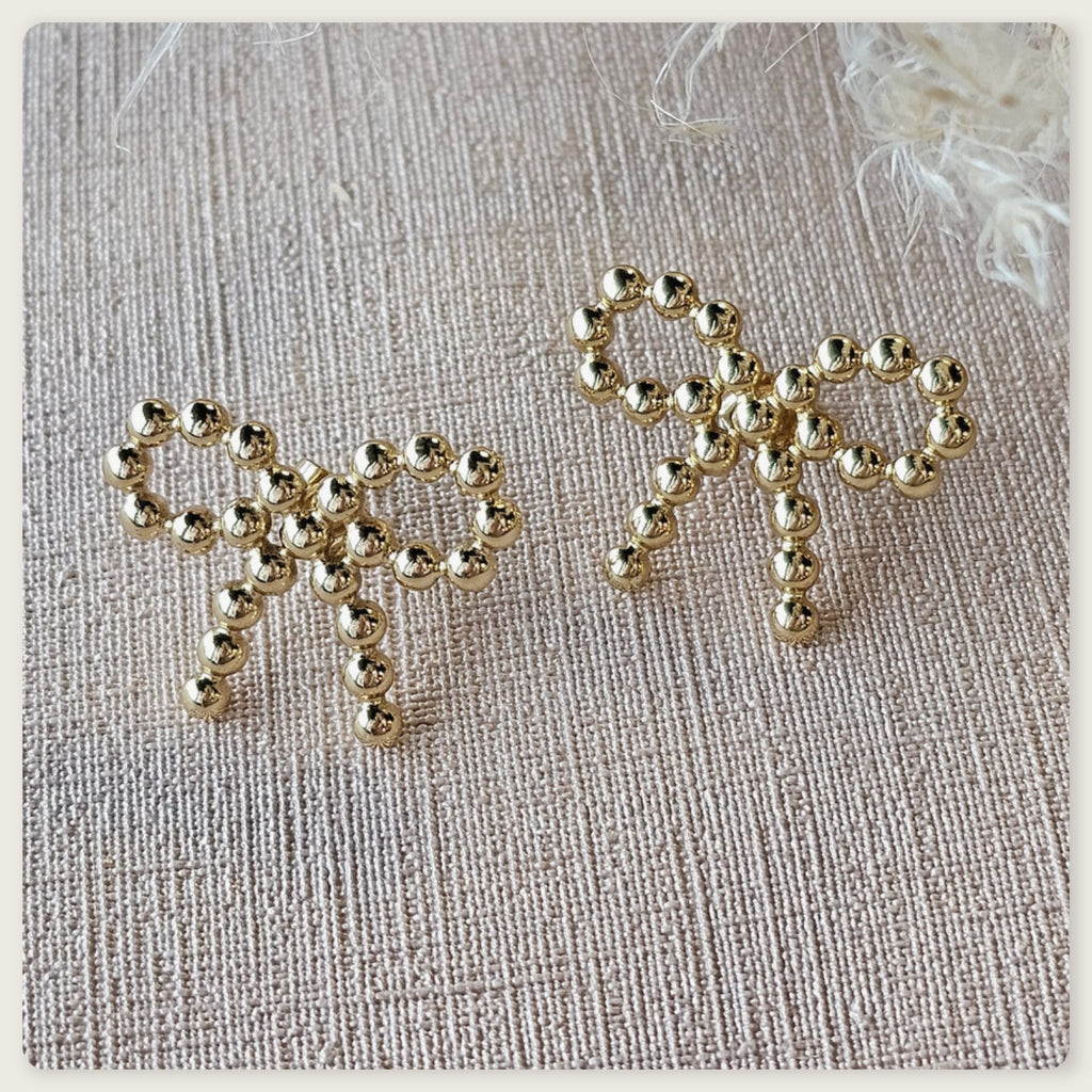 Seyso goudkleurige statement oorbellen in strikvorm met ronde bolletjes op lichte marmerlook achtergrond