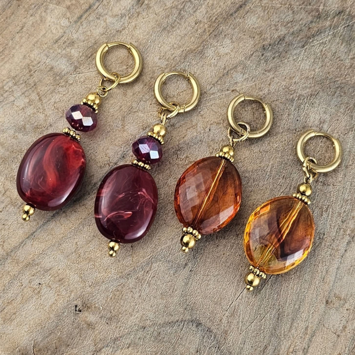 Close up van amberkleurige en bordeaux rode hangoorbellen met glanzende facetkralen, subtiele paarse kristallen en goudkleurige details.