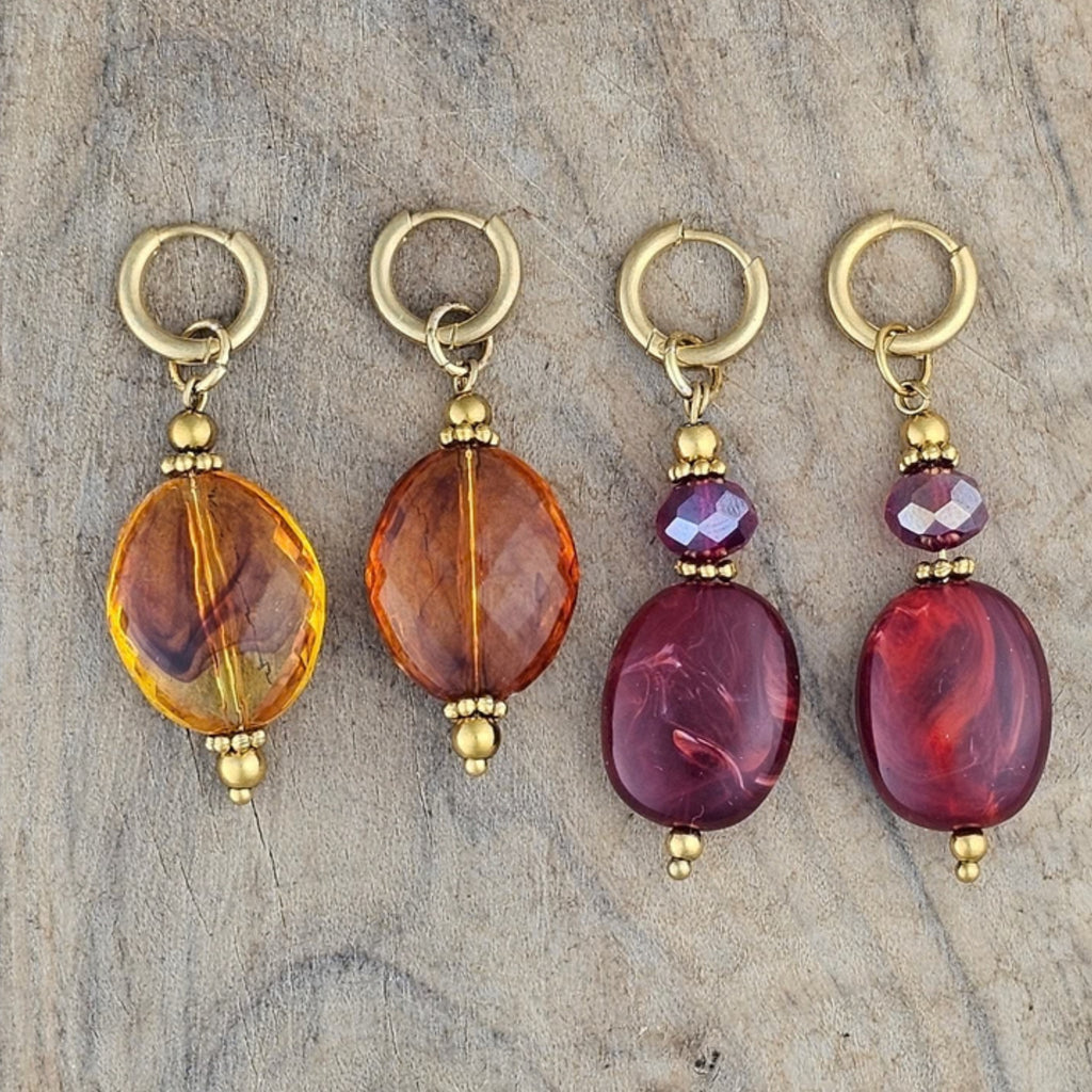 Twee paar amberkleurige oorbellen en twee paar bordeaux rode hangoorbellen met goudkleurige oorhaken en paarse kristallen van Seyso.