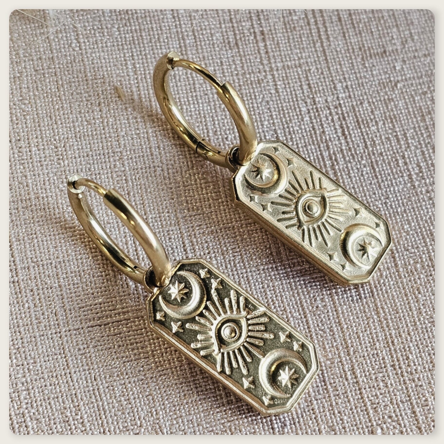 Seyso goudkleurige oorbellen met langwerpige hanger en gegraveerd oogmotief op lichte marmerlook achtergrond