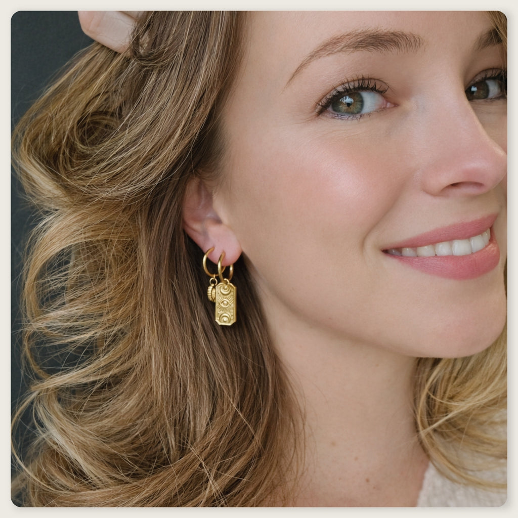 Seyso goudkleurige oorbellen met langwerpige hanger en gegraveerd oogmotief op lichte marmerlook achtergrond