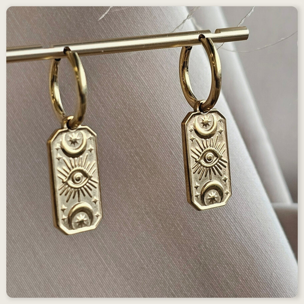 Seyso goudkleurige oorbellen met langwerpige hanger en gegraveerd oogmotief op lichte marmerlook achtergrond