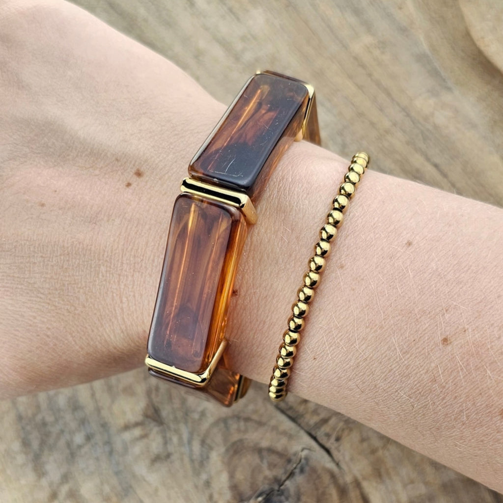 Bruin amberkleurige statement armband met gouden details gecombineerd met een goudkleurige kralen armband