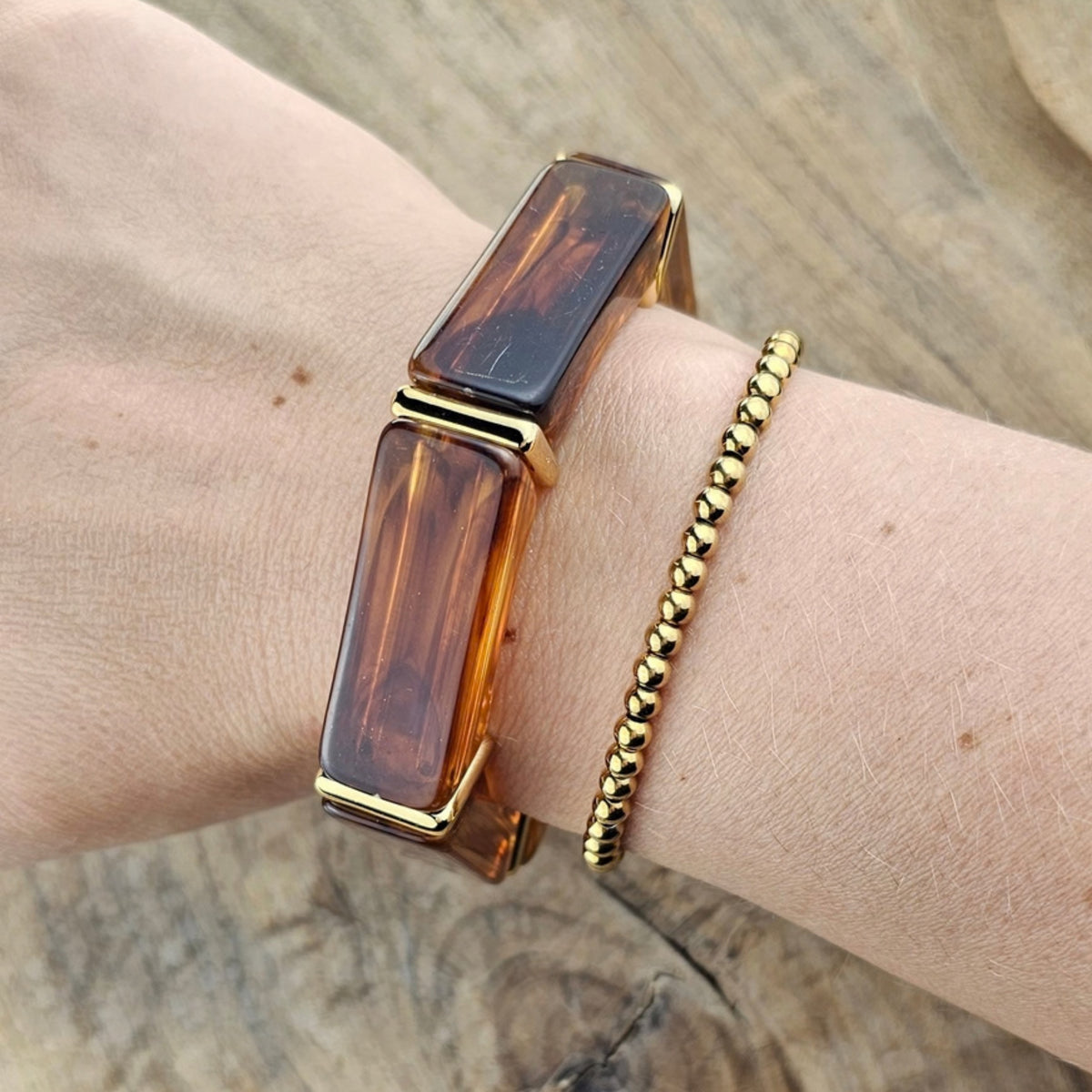 Bruin amberkleurige statement armband met gouden details gecombineerd met een goudkleurige kralen armband