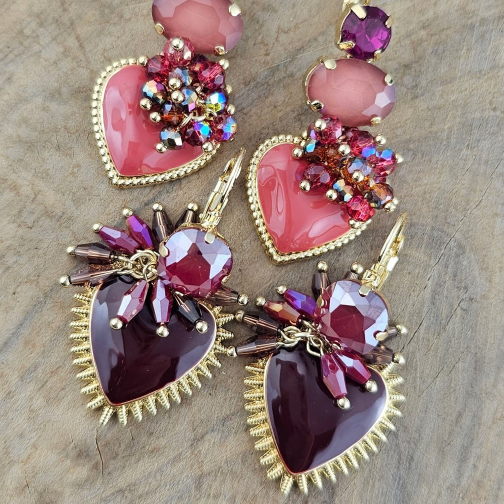 Kleurrijke statement oorbellen met roze en paarse hartvormige hangers, siersteentjes en goudkleurige details uit de Burgundy Bloom collectie.