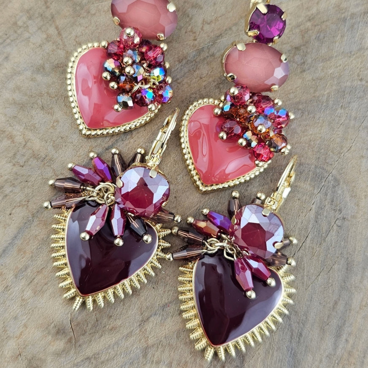 Kleurrijke statement oorbellen met roze en paarse hartvormige hangers, siersteentjes en goudkleurige details uit de Burgundy Bloom collectie.