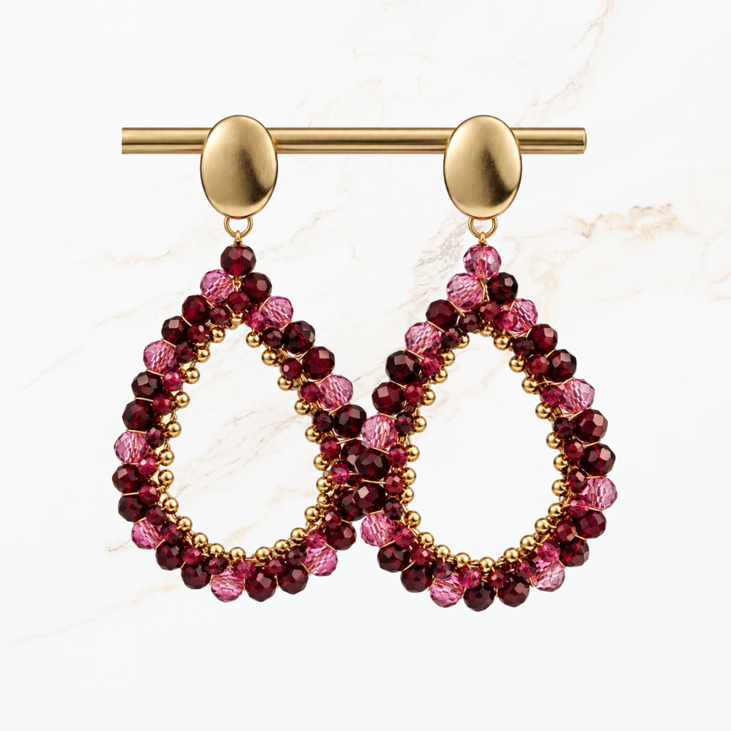 Bordeaux rode druppel oorbellen met fonkelende paarse en rode kralen, goudkleurige ovale oorstekers en open druppelvorm. Elegante sieraden van Seyso.