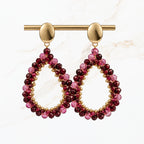 Bordeaux rode druppel oorbellen met fonkelende paarse en rode kralen, goudkleurige ovale oorstekers en open druppelvorm. Elegante sieraden van Seyso.