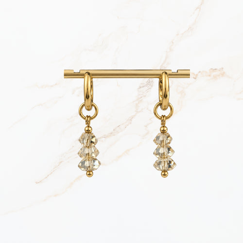 Elegante goudkleurige hangoorbellen met transparante gefacetteerde kristalkralen en subtiele gouden details. Stijlvolle dames oorbellen van Seyso.