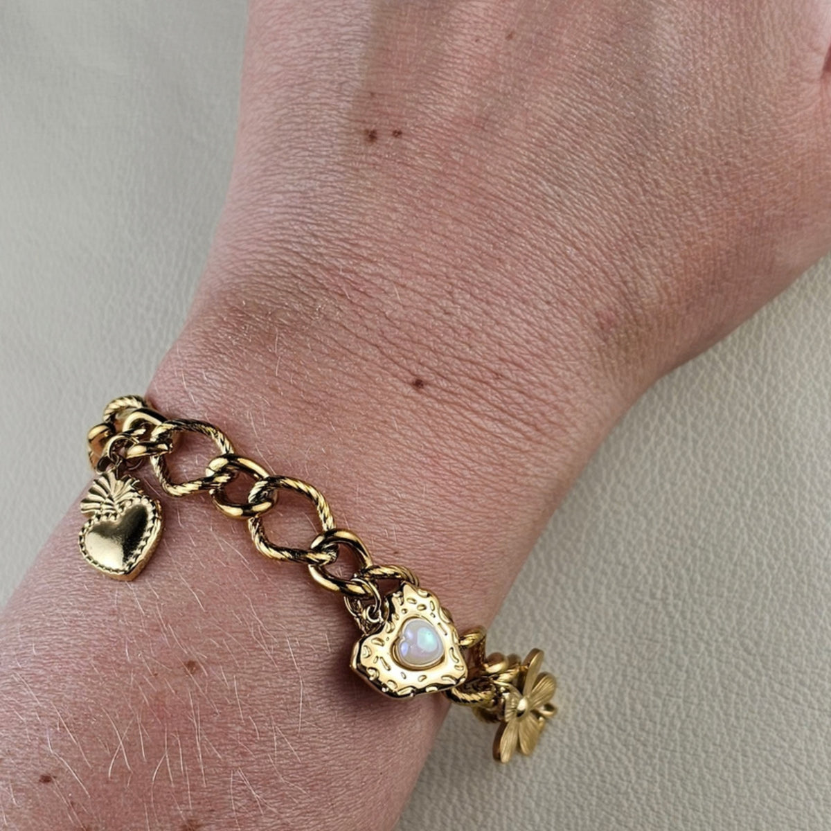 Gouden dames armband met hartjes bedels en bloem detail gedragen om de pols
