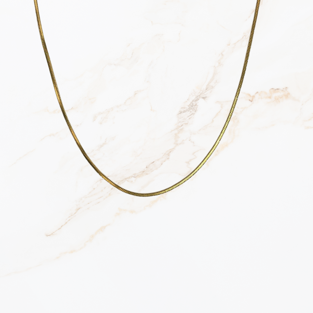 Goudkleurige snake chain ketting voor het zelf samenstellen van een ketting met verwisselbare bedels op lichte marmer achtergrond.