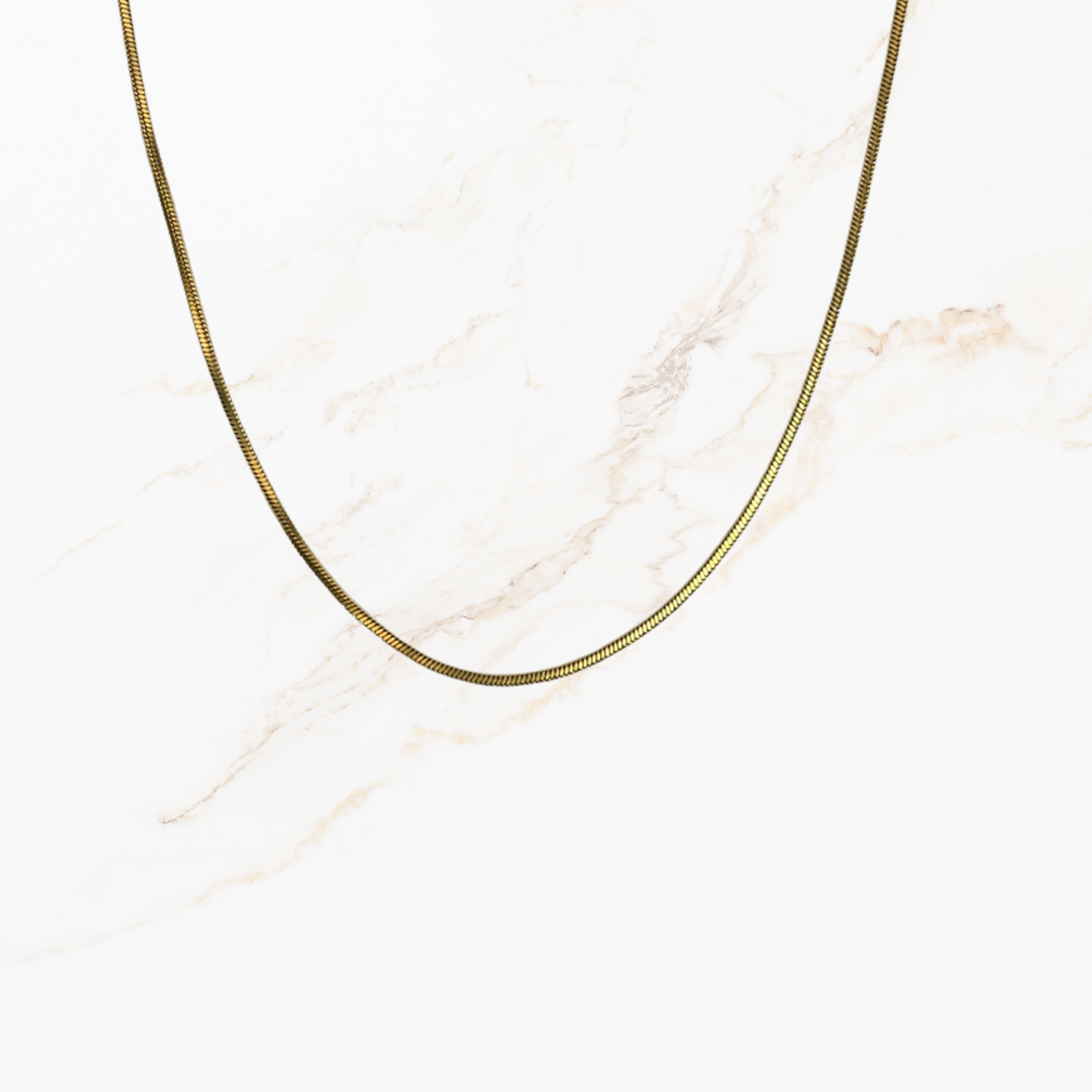 Goudkleurige snake chain ketting voor het zelf samenstellen van een ketting met verwisselbare bedels op lichte marmer achtergrond.