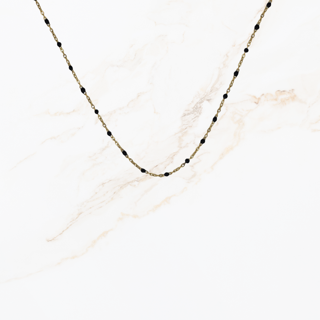 Goudkleurige ketting met kleine zwarte kraaltjes voor het samenstellen van een ketting met bedels op lichte marmer achtergrond.