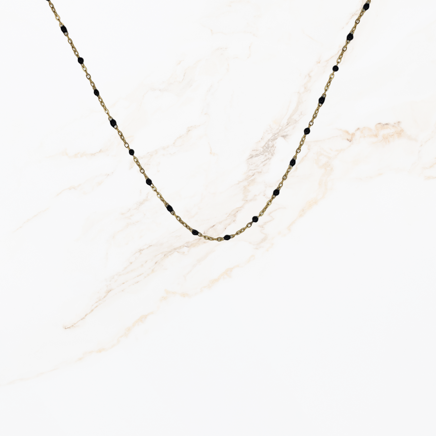 Goudkleurige ketting met kleine zwarte kraaltjes voor het samenstellen van een ketting met bedels op lichte marmer achtergrond.