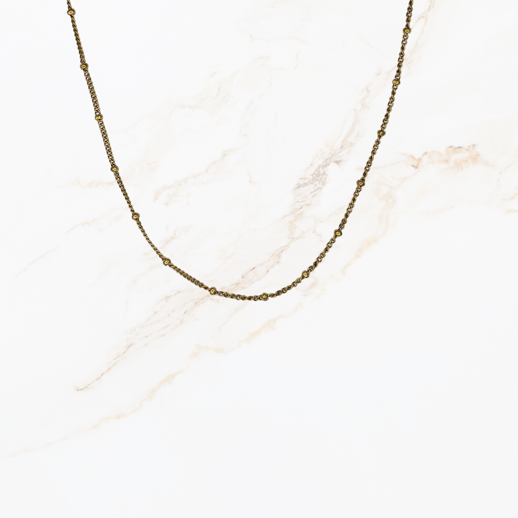 Fijne goudkleurige ketting met kleine bolletjes voor het samenstellen van een persoonlijke ketting met bedels op lichte marmer achtergrond.