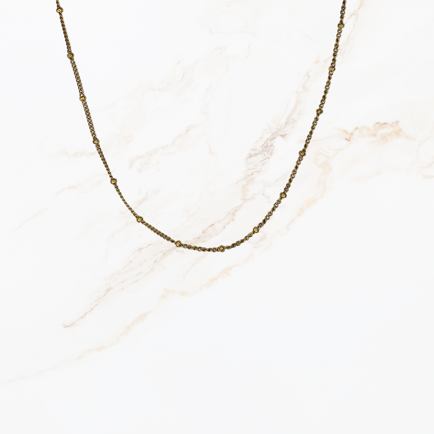 Fijne goudkleurige ketting met kleine bolletjes voor het samenstellen van een persoonlijke ketting met bedels op lichte marmer achtergrond.
