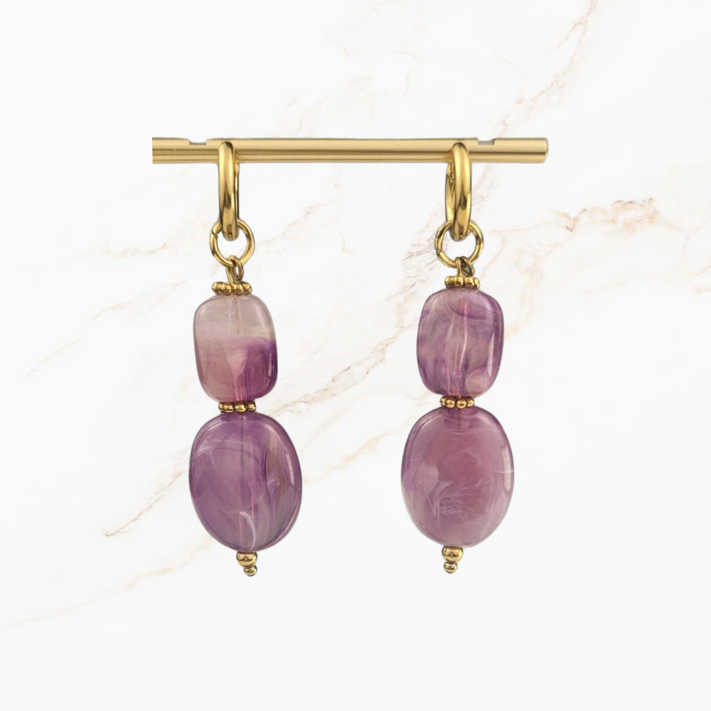 Elegante lila hangoorbellen met twee paarse glaskralen, goudkleurige oorhaken en verfijnde details. Handgemaakte dames oorbellen van Seyso.