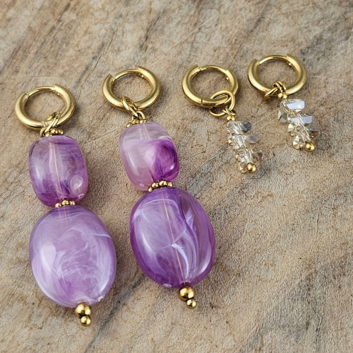 Twee paar lila hangoorbellen naast transparante kristallen oorbellen met goudkleurige oorhaken. Elegante handgemaakte sieraden van Seyso.