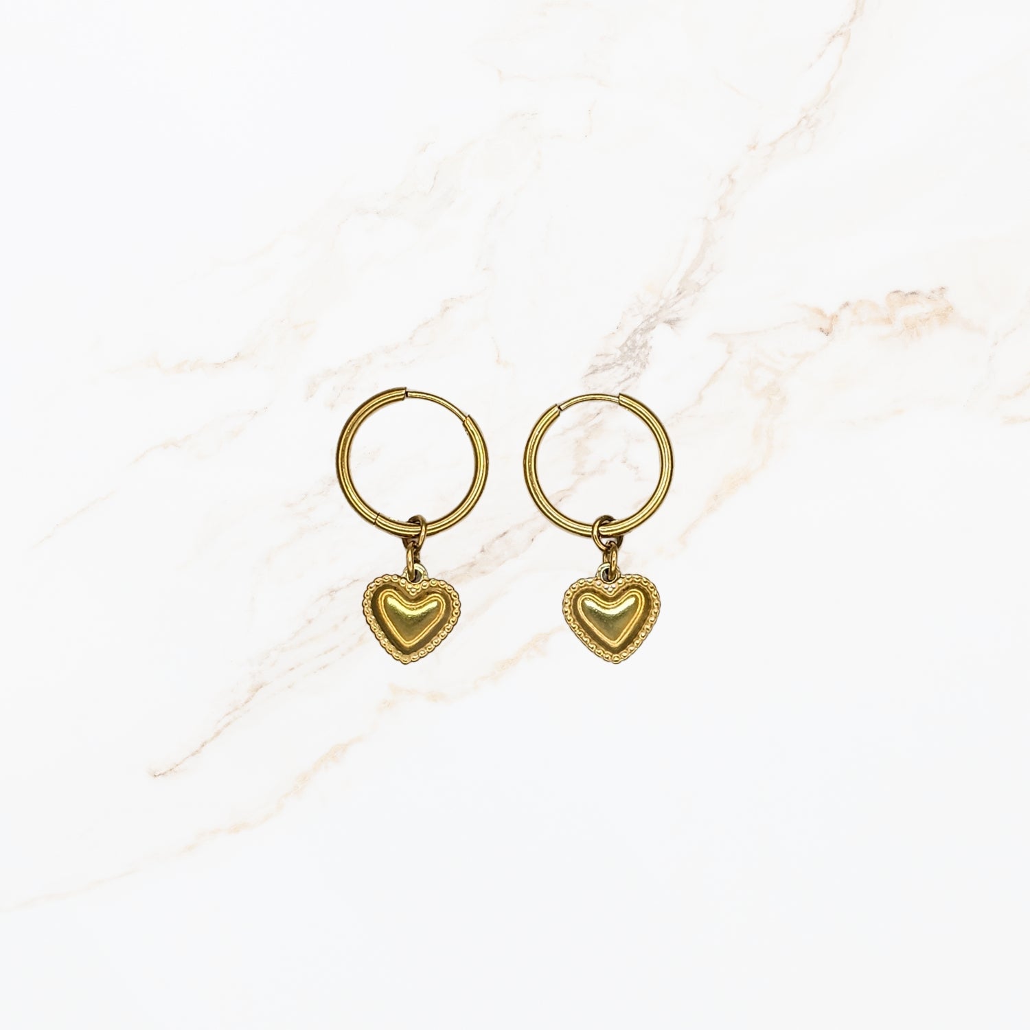 Seyso goudkleurige ring oorbellen met klein hartvormig hangertje op lichte marmerlook achtergrond