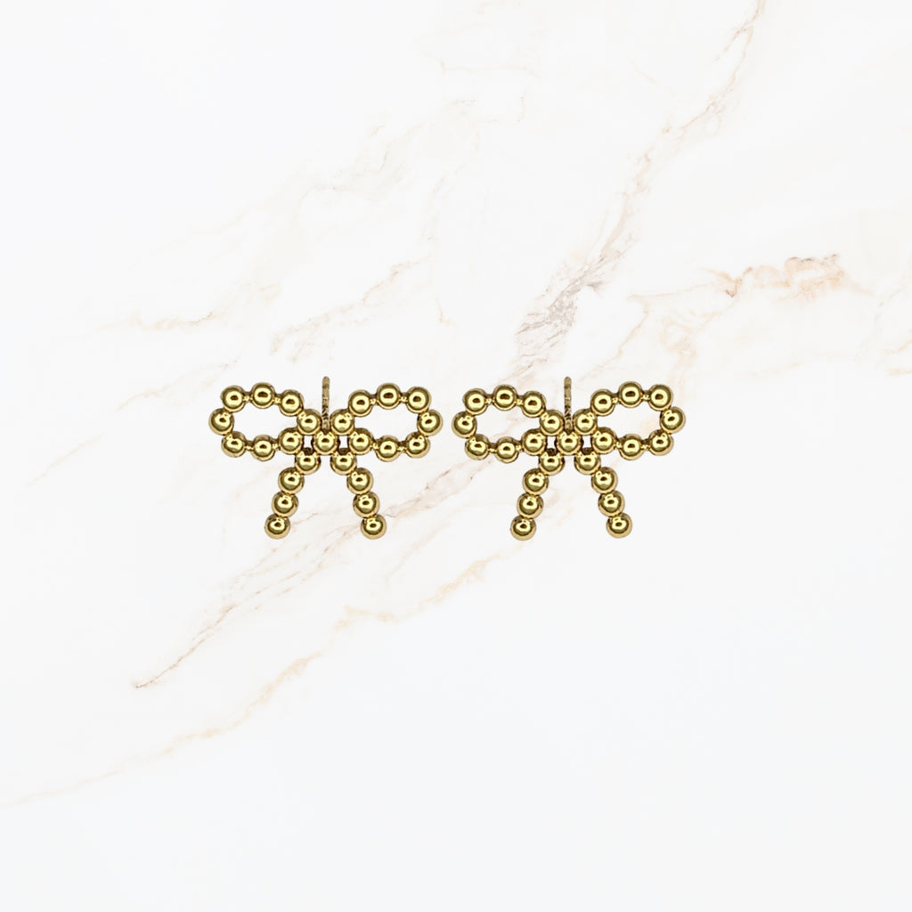 Seyso goudkleurige statement oorbellen in strikvorm met ronde bolletjes op lichte marmerlook achtergrond