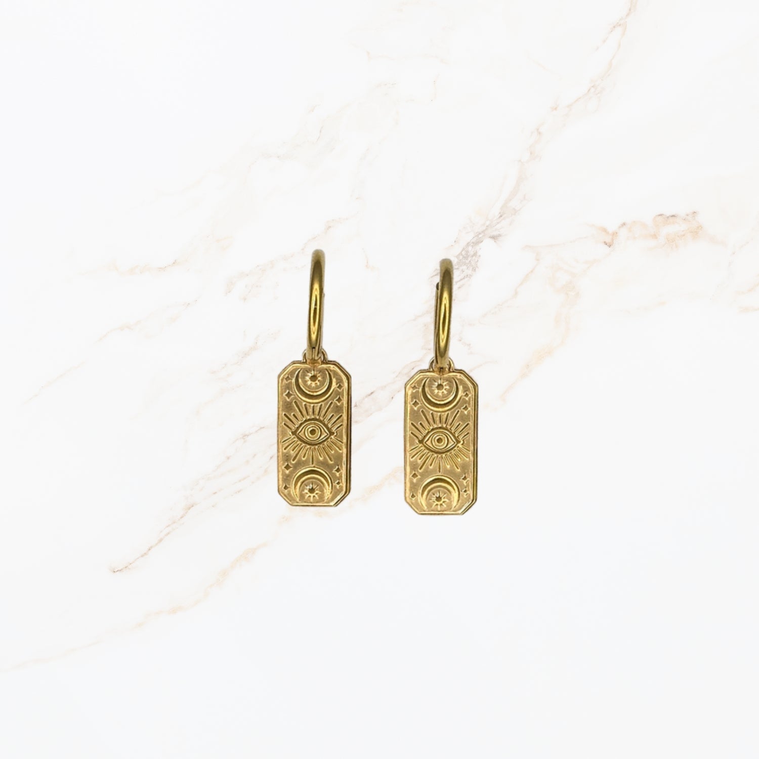 Seyso goudkleurige oorbellen met langwerpige hanger en gegraveerd oogmotief op lichte marmerlook achtergrond