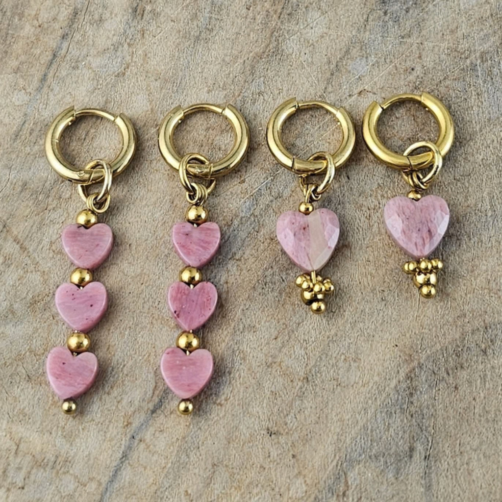 Verschillende lichtroze hartjes oorbellen met goudkleurige oorhaken, uitgevoerd met enkele en meerdere roze hartvormige hangers van Seyso.