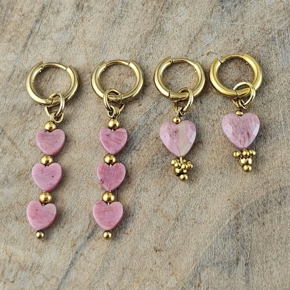 Verschillende lichtroze hartjes oorbellen met goudkleurige oorhaken, uitgevoerd met enkele en meerdere roze hartvormige hangers van Seyso.