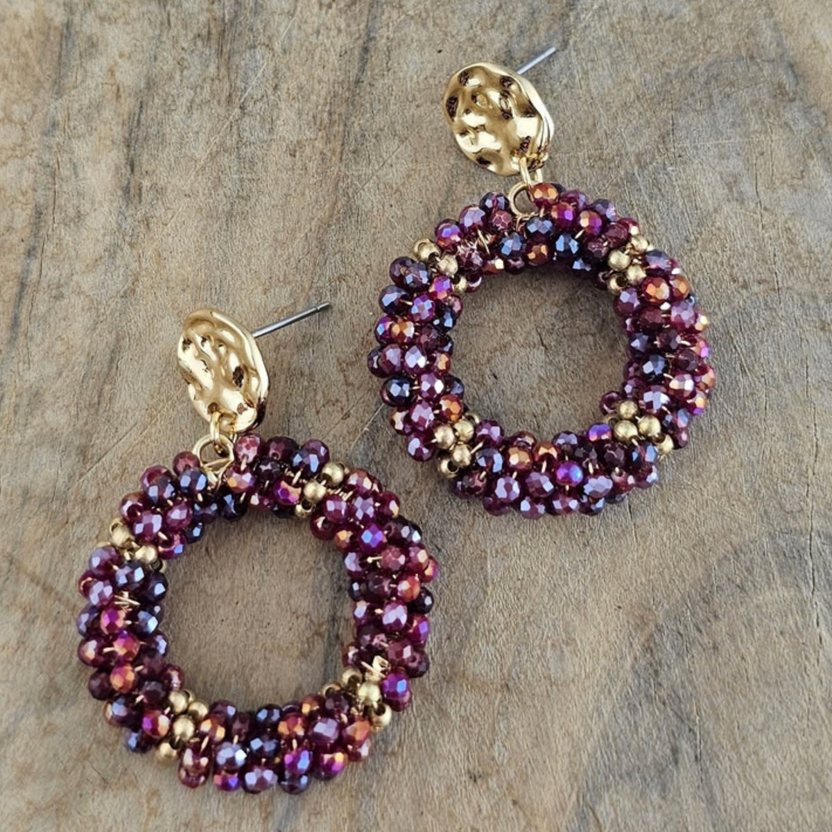Detail van ronde bordeaux rode statement oorbellen met glinsterende paarse kristalkralen en goudkleurige oorstekers, ideaal voor een feestelijke outfit.