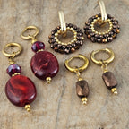Verschillende handgemaakte oorbellen in bordeaux rood, paars en goud met glanzende kralen en elegante hangers, perfect voor herfst en winter.