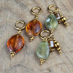 Handgemaakte hangoorbellen in zachtgroen en cognacbruin met ovale glaskralen, goudkleurige details en decoratieve hangers van Seyso.