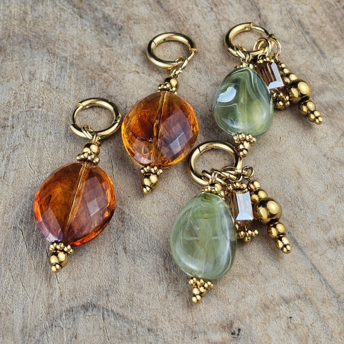 Handgemaakte hangoorbellen in zachtgroen en cognacbruin met ovale glaskralen, goudkleurige details en decoratieve hangers van Seyso.