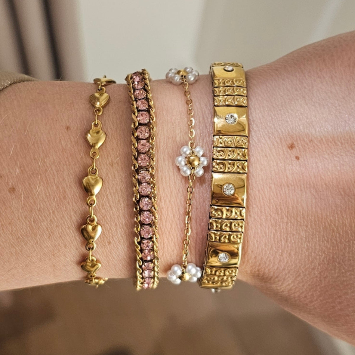 Goudkleurige bloemen armband gecombineerd met meerdere fijne dames armbanden